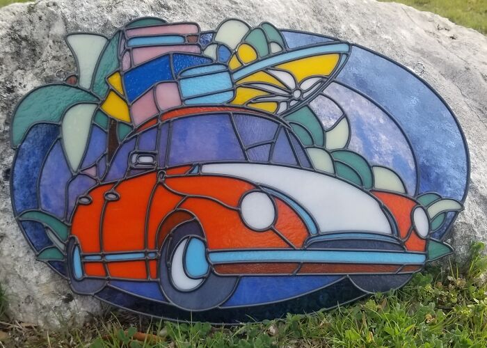 Stained glass art of a colorful vintage car piled with luggage and tropical leaves, showcasing pop culture icons.