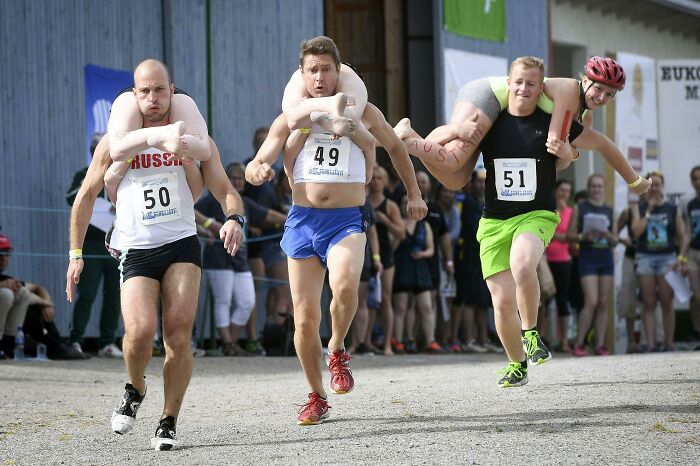 Men participating in a strange tradition of carrying wives in a race, showcasing bizarre traditions from around the world.