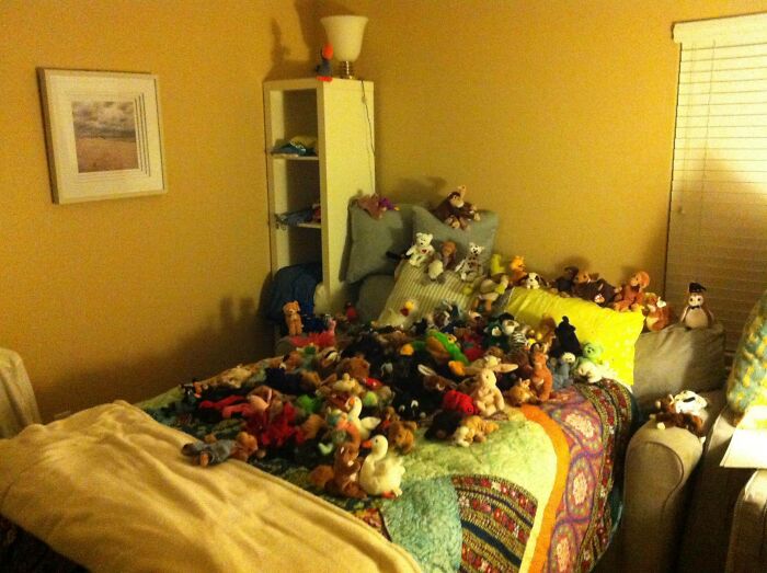 A cluttered bedroom filled with numerous stuffed animals scattered on the bed, showing a messy roommate situation.