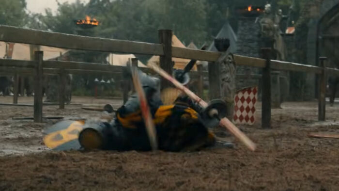 Knight falls during a medieval jousting tournament, with house sigils visible on shields and banners in the background