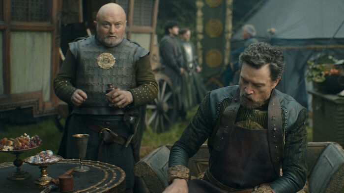 Two men in medieval attire inside a camp setting, representing characters from every house sigil in a Knight of the Seven Kingdoms.