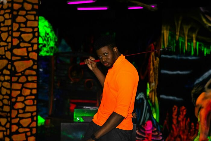 Man in bright orange shirt striking a bold pose in a dark, neon-lit setting showing weird things people did in public.