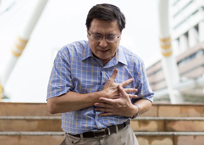Middle-aged man in glasses clutching chest in pain, illustrating heartbreaking and sad goodbyes at the airport.