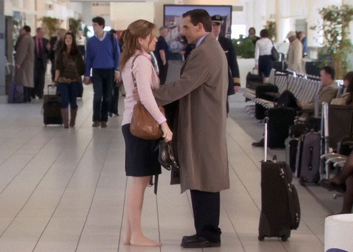 Couple sharing a heartfelt and sad goodbye at the airport terminal surrounded by travelers and luggage.
