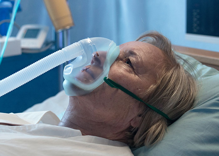 Elderly woman in a hospital bed wearing an oxygen mask, conveying a heartbreaking and sad farewell moment.