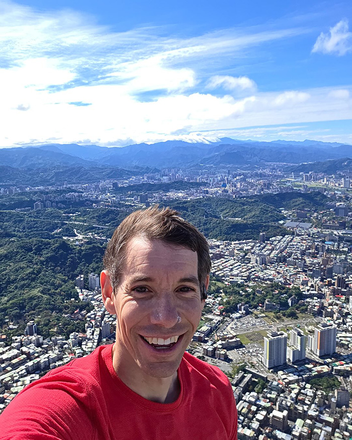 Famous climber taking a selfie above a cityscape highlighting low pay controversy for Netflix skyscraper climb.