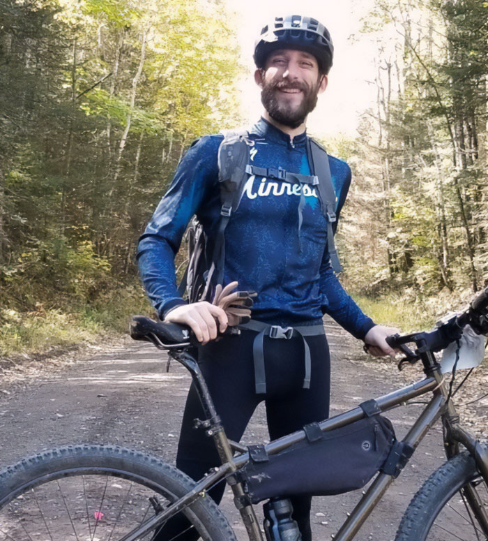 Man with a bike smiling outdoors in forest, representing Alex Pretti&rsquo;s parents learning his fate from a reporter.