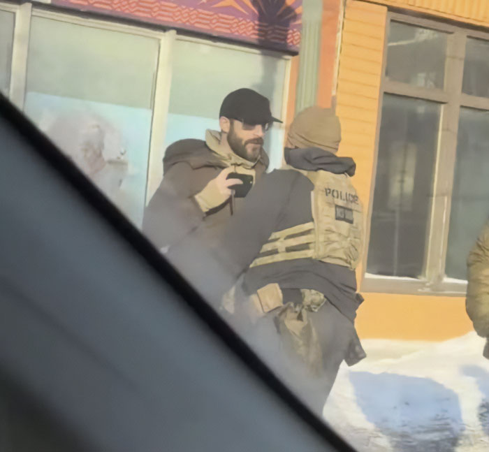 Man wearing a black cap talking with a police officer outside a building in snowy weather during daylight.