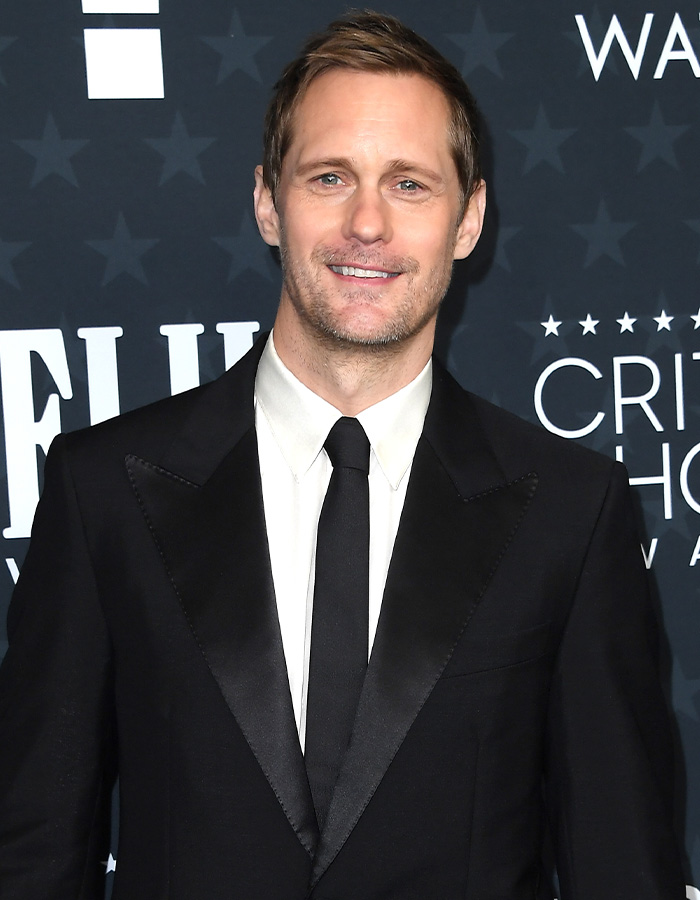 Alexander Skarsg&aring;rd at an event, wearing a black suit and tie, addressing orientation after viral comments.