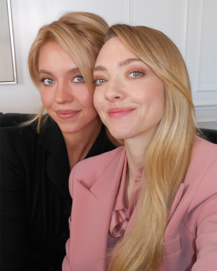 Amanda Seyfried smiling with a friend, dressed in pink and black, capturing a casual moment amid Golden Globes reactions.