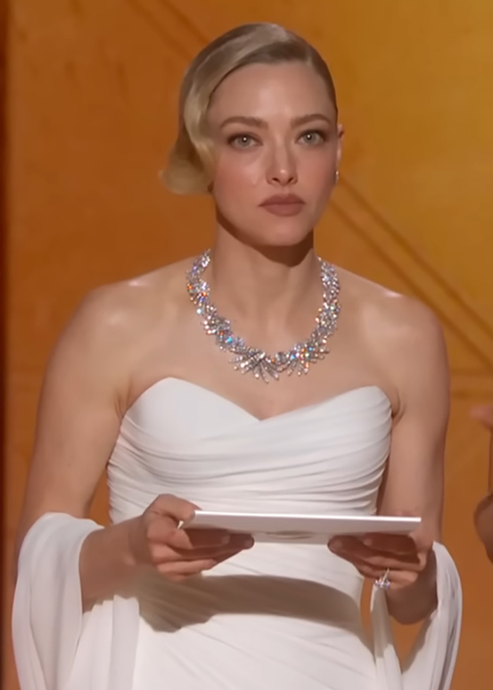 Amanda Seyfried in a white gown and sparkling necklace, showing a serious expression during Golden Globes event.