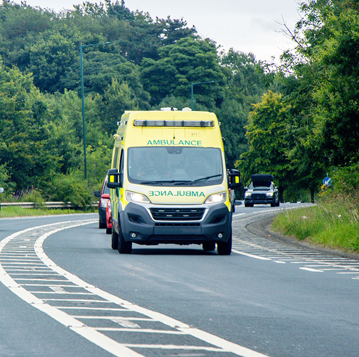 Yellow ambulance driving on a curved road surrounded by trees, symbolizing an emergency call situation at night.