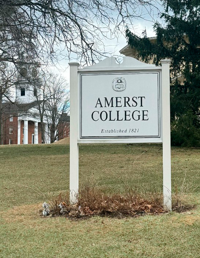 Amherst College sign on campus lawn with historic building and trees in the background amid firing spree controversy. Amherst College sign on campus lawn with historic building and trees in the background amid firing spree controversy.