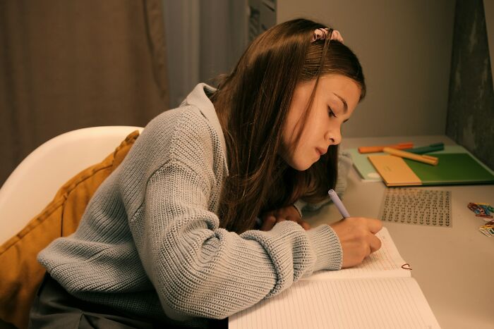 Teenage girl focused on writing at desk in a high school setting, illustrating education amid potential controversies.