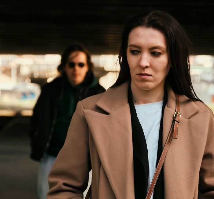 Woman looking concerned while walking outside with a man behind her, illustrating women feeling safer living alone.