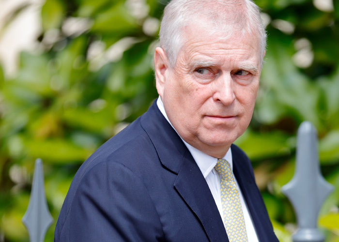 Prince Andrew outdoors in a navy suit and yellow tie, with green foliage in the background, revealing country move after eviction.