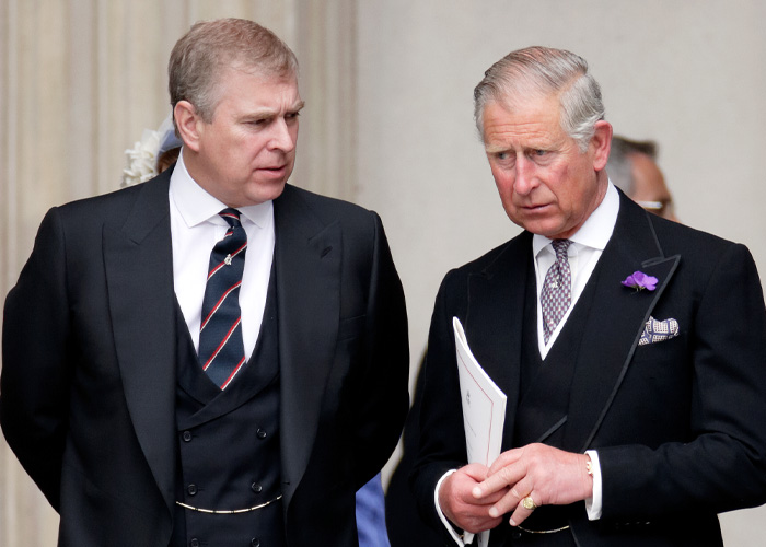 Prince Andrew dressed in a black suit standing beside another man in a black suit during a formal event.