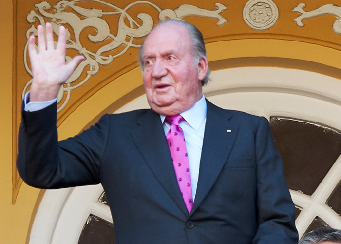 Elderly man in a suit raising his hand, symbolizing royal author discussing Prince Andrew's new country after eviction.