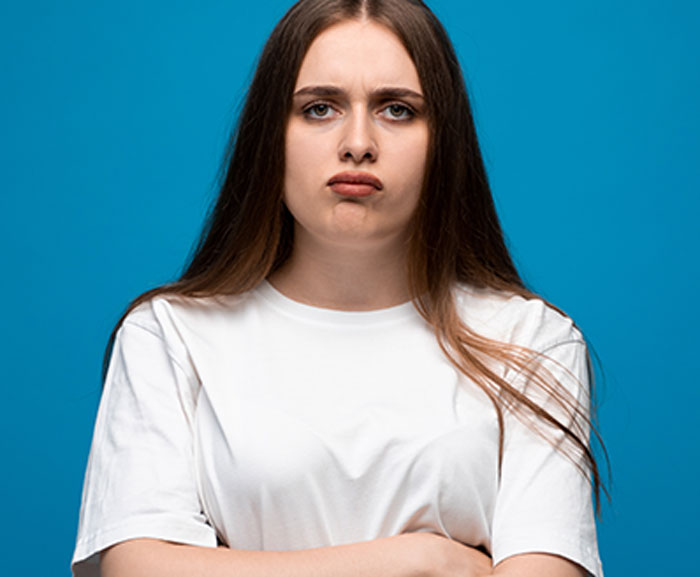 Young woman with long hair and crossed arms expressing frustration about husband&rsquo;s relatives living with them