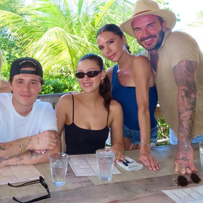 Victoria Beckham and Nicola Peltz posing together with two others at a table outdoors during a casual outing.