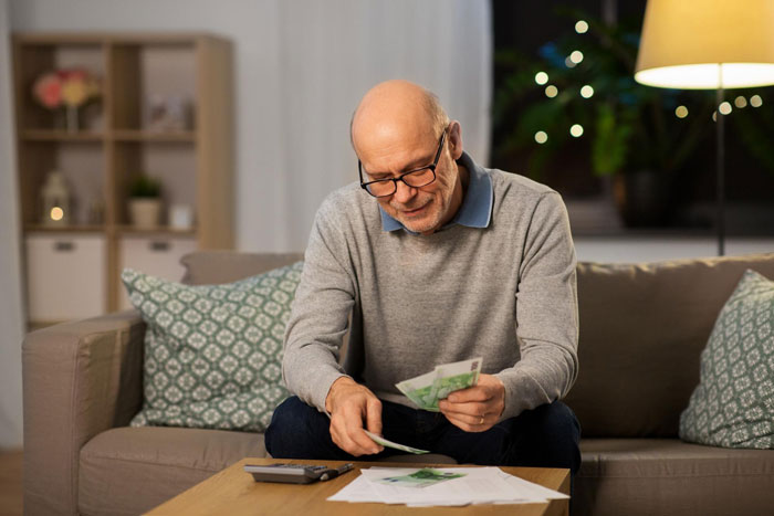 Elderly man counting cash at home with calculator and bills, concerned about parents house payment