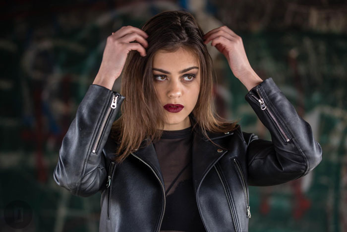 Young woman in a black leather jacket adjusting hair, posing confidently with a camera-ready look in an urban family setting. Young woman in a black leather jacket adjusting hair, posing confidently with a camera-ready look in an urban family setting.
