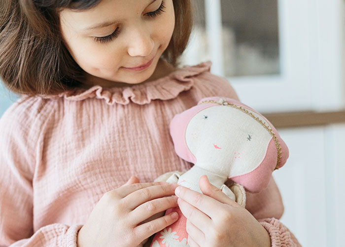 Young girl in pink dress holding a soft doll, related to babysitter gift and mother furious story context.
