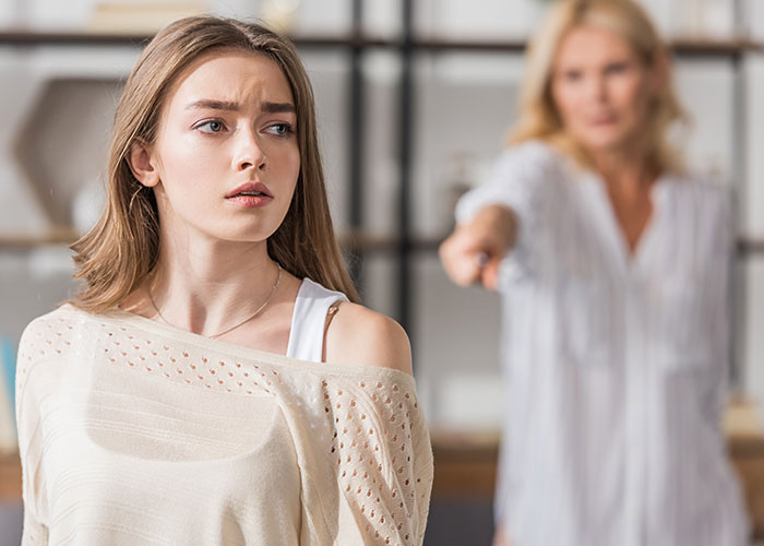 Young babysitter looks concerned while mother angrily points at her in a tense moment at home.