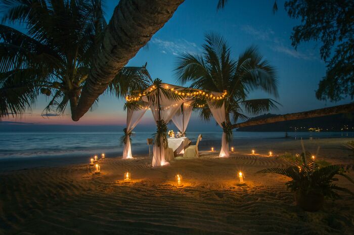 Romantic beach dining setup at sunset with candles and palm trees, illustrating meaningful dating gestures.