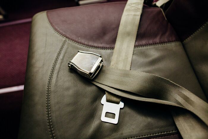 Airplane seatbelt clasp resting on a brown and gray leather seat, symbolizing minimal dating gestures to accept.