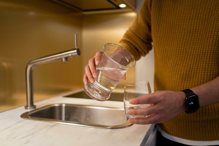 Person in mustard sweater pouring water into a glass, illustrating simple dating gestures and minimal effort.