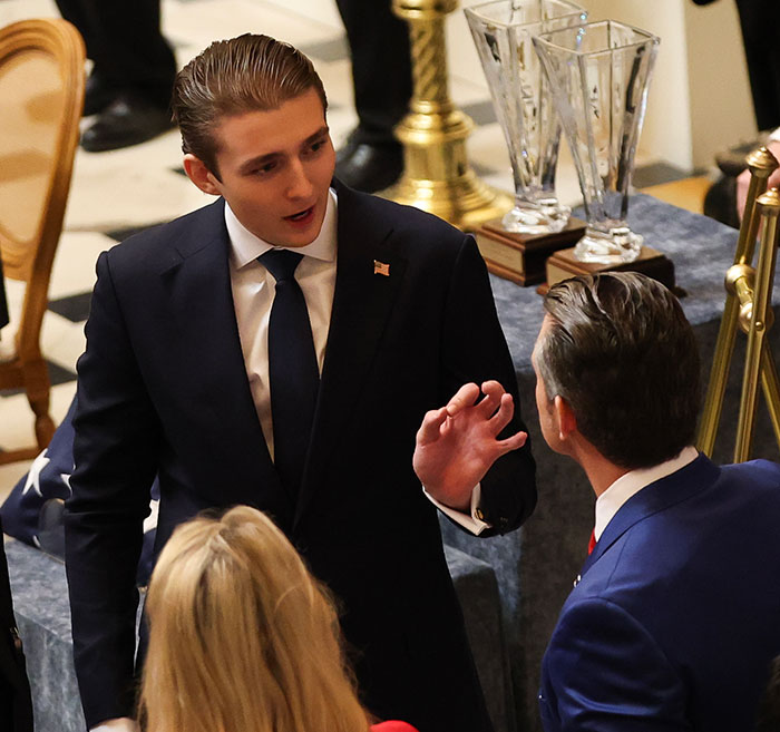 Barron Trump speaking with two people in suits at a formal event, engaged in conversation during emergency call discussion.