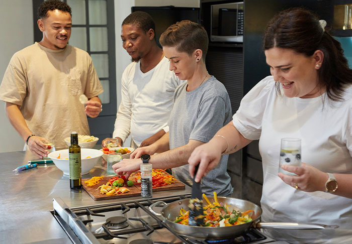 Four friends cooking together in a kitchen, practicing easy skills to improve life and prepare healthy meals.