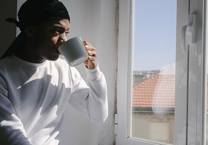 Man drinking coffee near window in natural light, reflecting on easy skills to improve your life and retire rich.