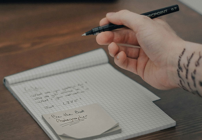Hand holding a pen over a notebook with notes, focusing on easy skills to improve your life and retire rich.