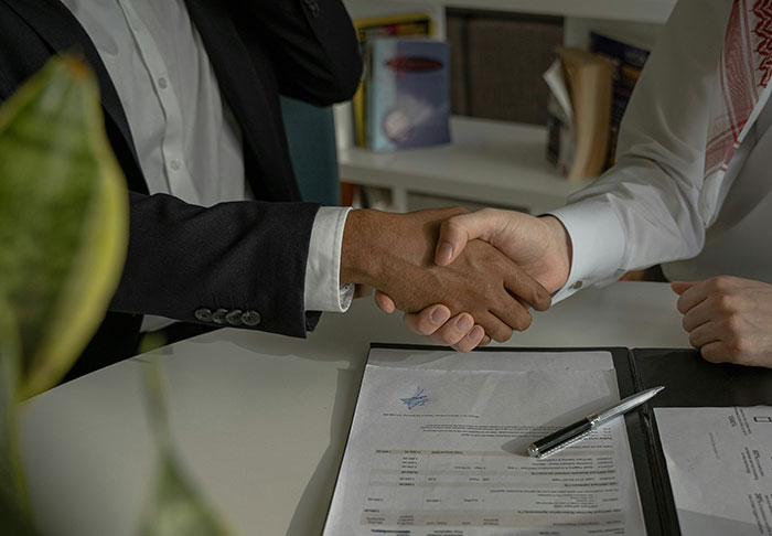 Two professionals shaking hands over a signed contract, symbolizing skills to improve your life and financial success.