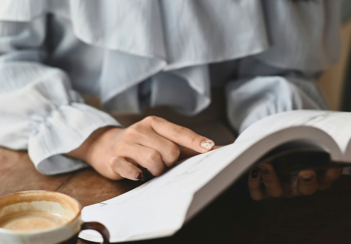 Person reading a book focused on skills to improve life, with a cup of coffee on a wooden table nearby.