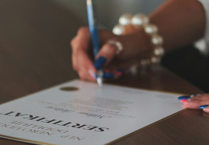 Person with blue nails and pearl bracelet signing a financial document focused on skills to improve your life.