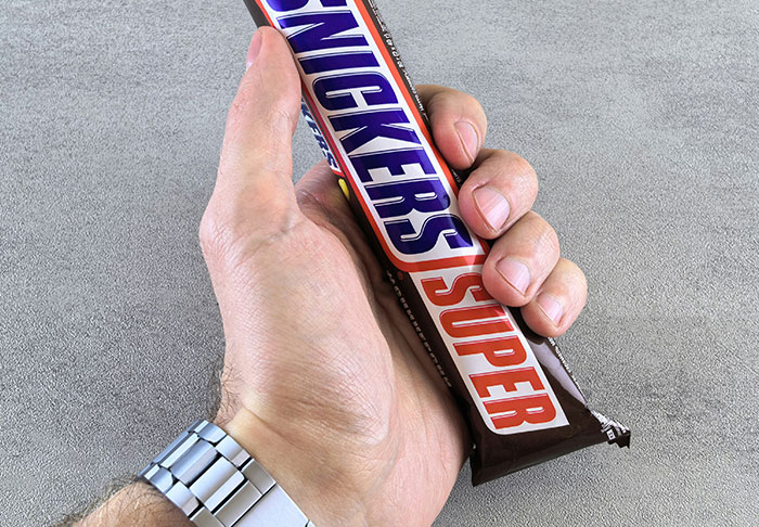 Hand holding a Snickers Super chocolate bar, illustrating easy skills to improve your life and achieve financial success.