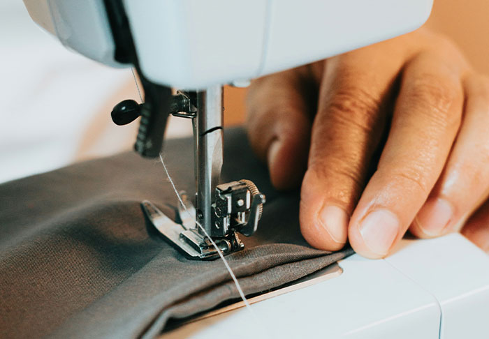 Close-up of hands guiding fabric through a sewing machine, illustrating easy skills to improve your life and retire rich.