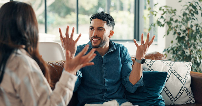 Man and woman having a serious conversation on couch, illustrating conflict with religious and unreligious beliefs.