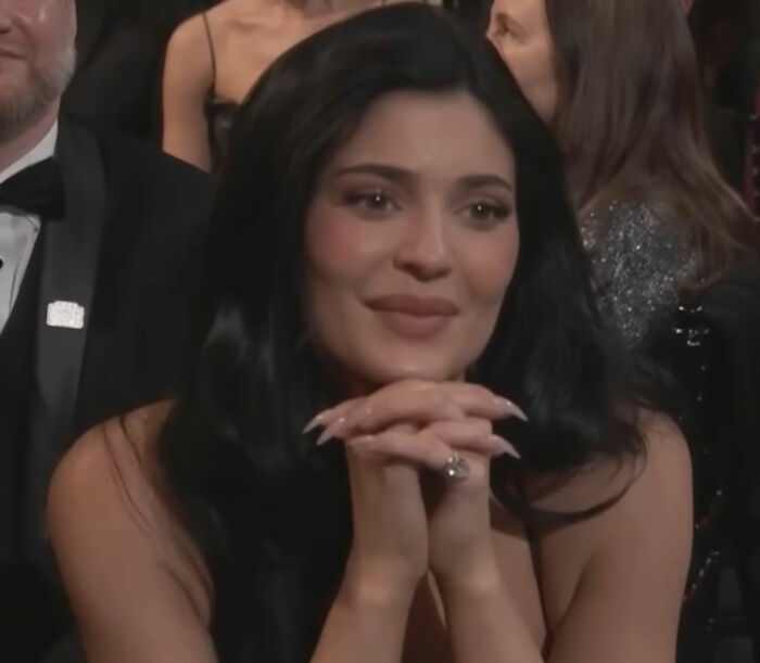 Woman with long black hair and manicured nails sitting at an event, related to video of Timoth&eacute;e Chalamet using Kylie's BBL.