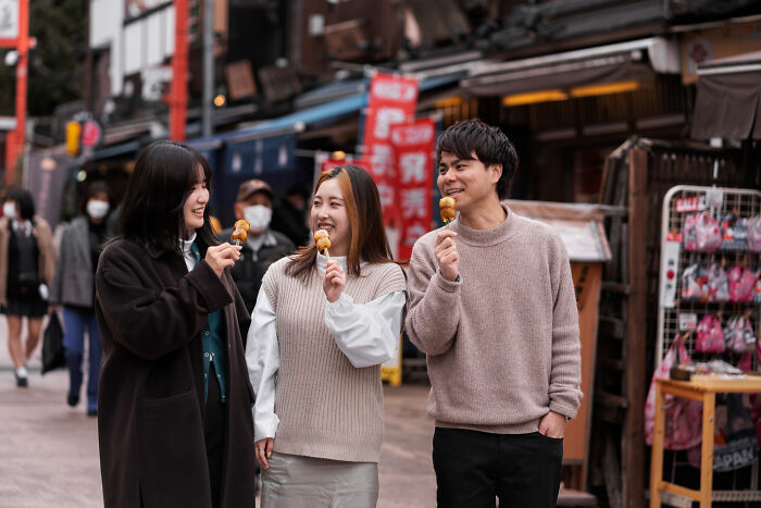 Three young bilingual people enjoying street food while walking, capturing awkward instances of gossiping moments.