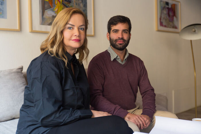 Two bilingual people sitting on a couch looking at the camera in a casual indoor setting.