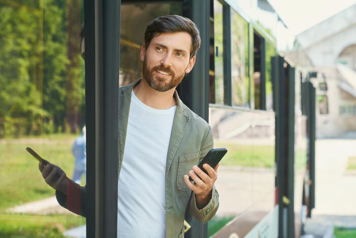 Man using smartphone while peeking from bus door, illustrating awkward bilingual moments catching gossip.