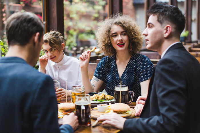 Group of bilingual friends having a meal, awkwardly catching someone gossiping in a casual restaurant setting.