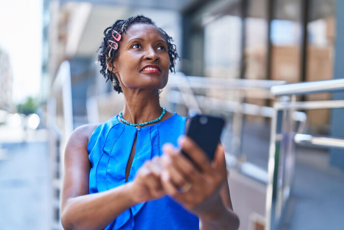 Woman in blue top using smartphone outside, capturing weird and awkward moments bilingual people catch gossiping.