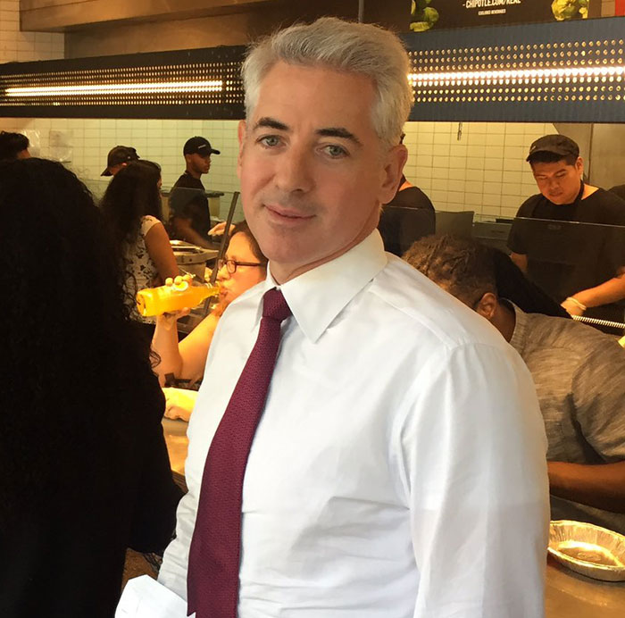 Bill Ackman wearing white shirt and red tie in a busy restaurant, linked to billionaires and donation controversy.