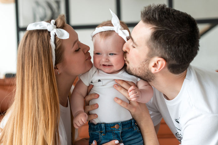 Young parents kissing their smiling baby girl, highlighting bio mom appears after 16 years in family reunion moment.