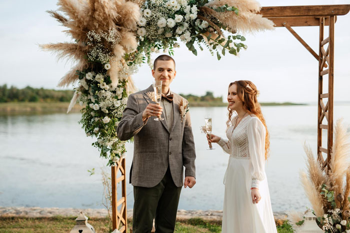 Couple celebrating wedding day under floral arch by the water, highlighting ownership clash over wedding date conflict. Couple celebrating wedding day under floral arch by the water, highlighting ownership clash over wedding date conflict.